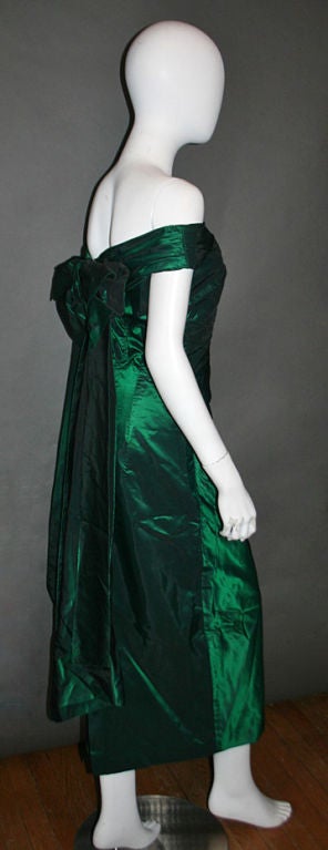 This gorgeous gown is composed of shimmering emerald green silk taffeta fabric. Gathered shoulders and a plunging v-neckline. Gathered bodice and full-length straight skirt. Beautiful, oversized bow with long with long, pleated, silk panel extending