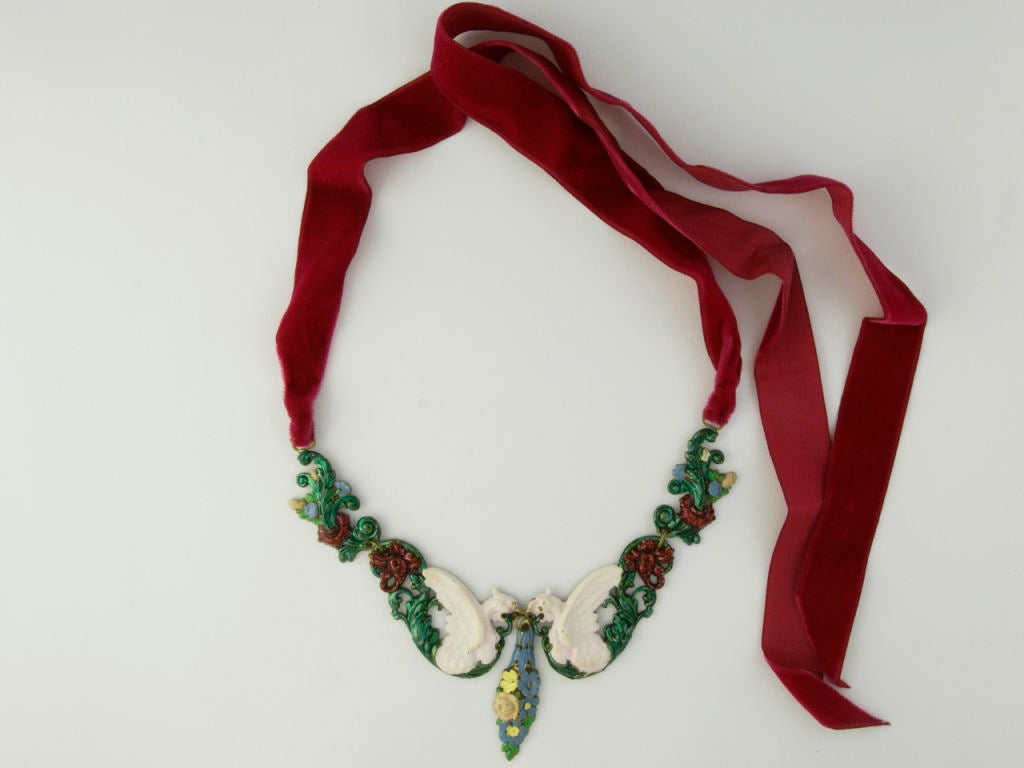 Two facing griffins holding a pendant representing a cluster of flowers and surrounded by naturalistic ornamental motifs are attached to two shocking pink silk velvet ribbons. This necklace has been shown in the exhibition 