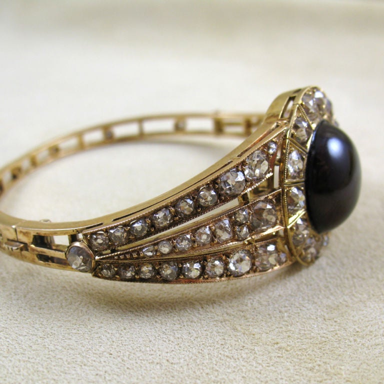 The hinged bangle of tapering design, with 3 lines of graduated old-mine diamonds on each side, centering on a garnet cabochon of circa 35 carats in a diamond frame, for a total of circa 8 carats of diamonds, mounted in 18kt yellow gold, inner