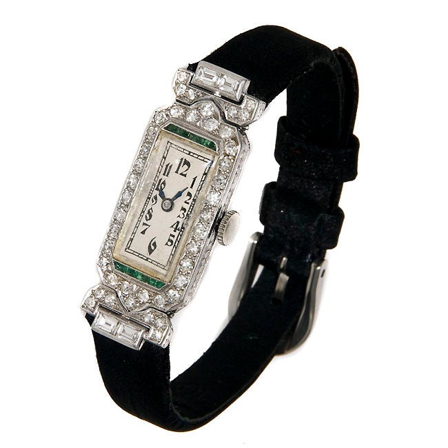 Ladies Art Deco Platinum watch by Glycine, set with Round and Baguette Diamonds and further accented with Emeralds. Movement is 17 Jewel manual wind.