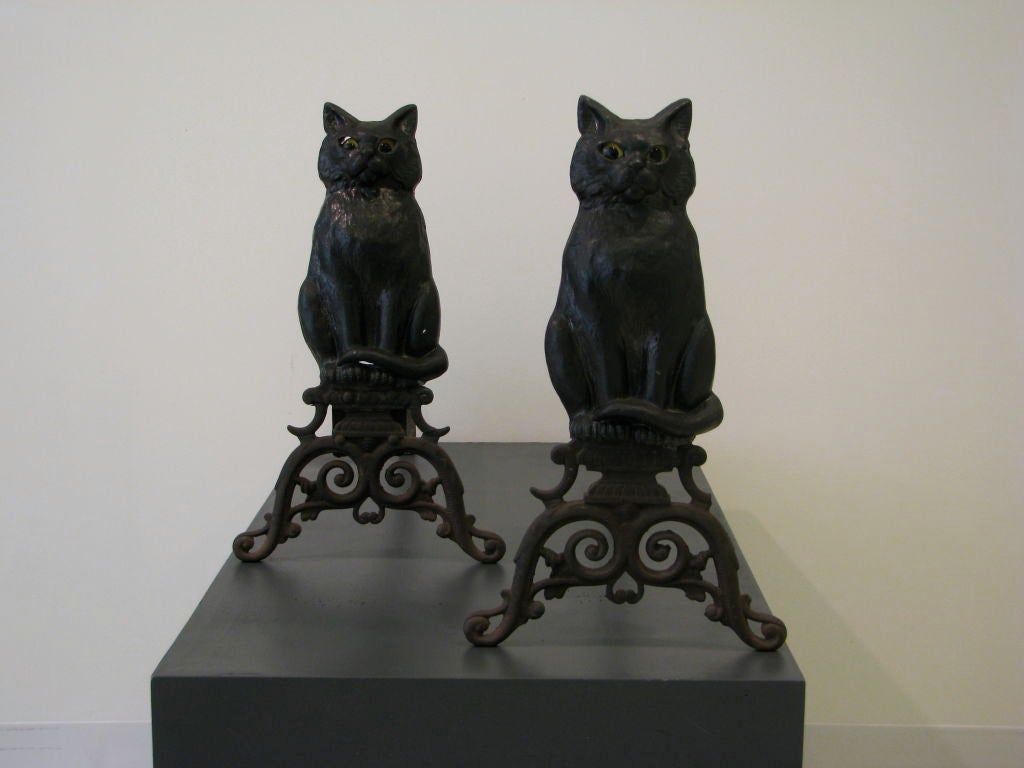 Pair of cast iron black cat andirons with yellow glass eyes. Rarely seen. Most often found in the form of an owl with yellow glass eyes. incredible form. The eyes tend to follow you around the room. <br />
each cat is 18