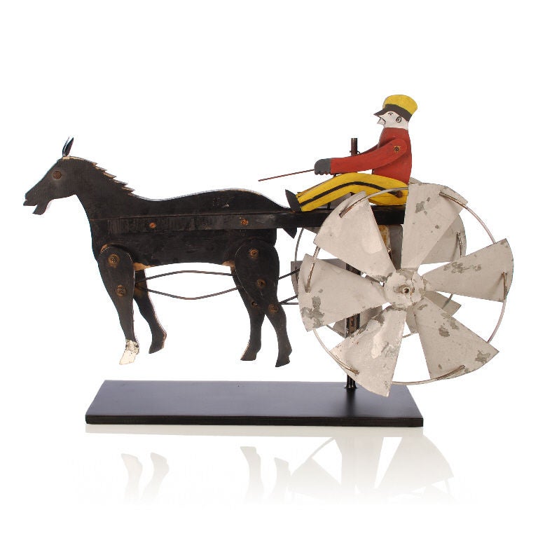 This is a wonderful American Folk Art Whirligig depicting Harness Racing, with its colorful driver sitting atop his horse drawn sulky. Great working mechanical piece. As the wind would blow the large windmill blade wheels, the drivers arm and whip