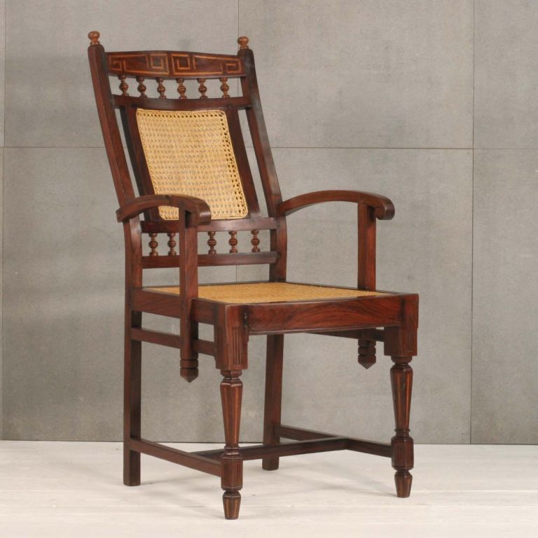 A pair of British Colonial armchairs in rosewood with a concave inset top rail with inlayed Greek key pattern. Short vertical turned splats are located on the top and bottom of the caned back. Square section arms curve gently into the back. Arms