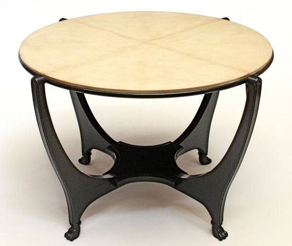 The circular top with one face veneered in pommele-figured sapele which rotates to reveal a parchement quartered top; raised above four graceful arching supports with paw feet centering a shaped shelf; By Hunzinger with embossed tin label under