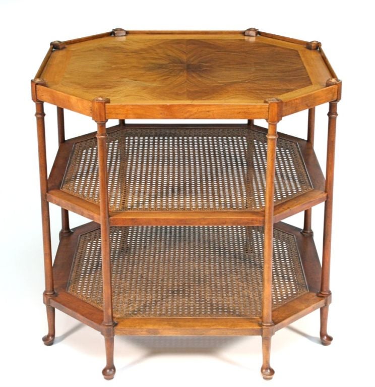 The top shelf with well-figured walnut book-matched veneers enclosed by a plain gallery; above two lower conforming shelves with cane insets; raised on eight turned supports of circular section with pad feet; the warm walnut with sun fading.