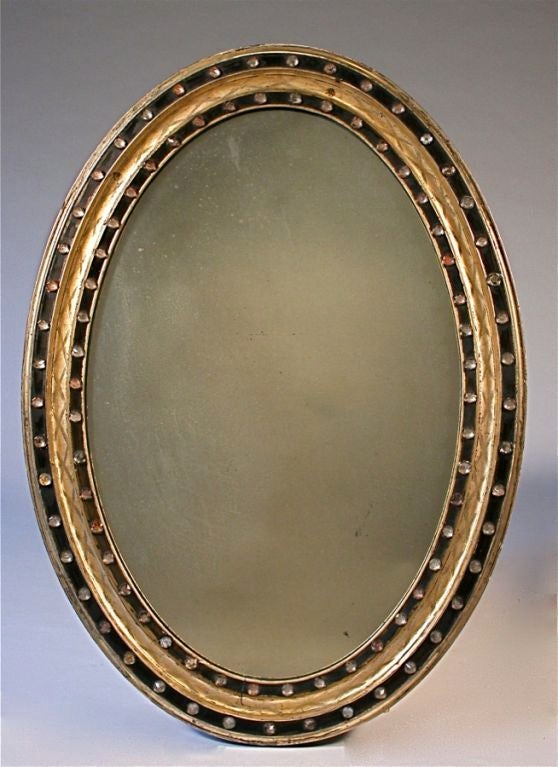 Of oval form; the bolection molding with a cross-hatched patterning in the larger white gold leaf border; with glass stars as accents; with three ebonized borders.