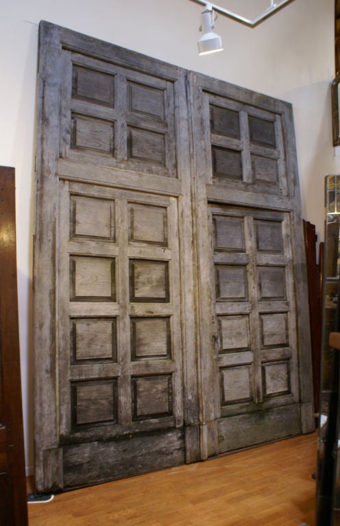 A massive pair of weathered chestnut winery doors made about 100 years ago in Northern Italy. Possibly used as front doors to a courtyard. The two large doors open. The door on the right side has the bottom panel hinged to open as a door. The