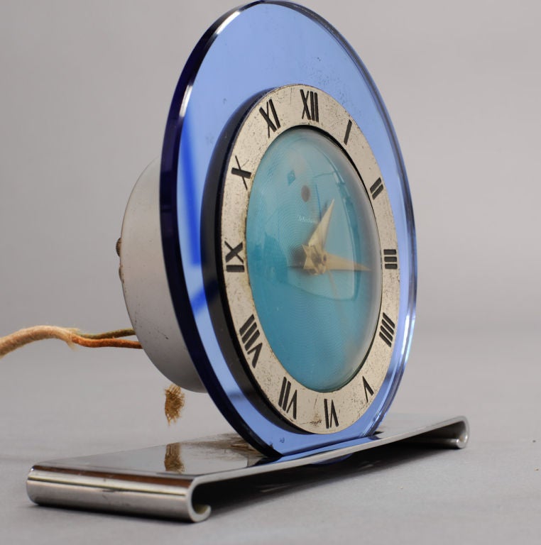 A beautiful desk clock with a wonderful blue glass face set into a chrome scrolled base.  The clock keep time.  The arms are arrowed and it has a rised number ring.