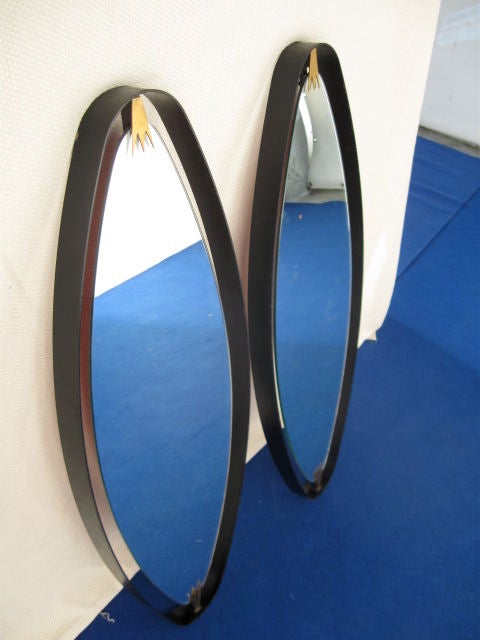 Early 40s brass and black lacquered iron oval mirrors. Quite a unique pair in the fact that the oval frame is obtained from a single curved iron plate with two elegant manufactured brass elements joining the mirror to the frame. Mirror, mirror on
