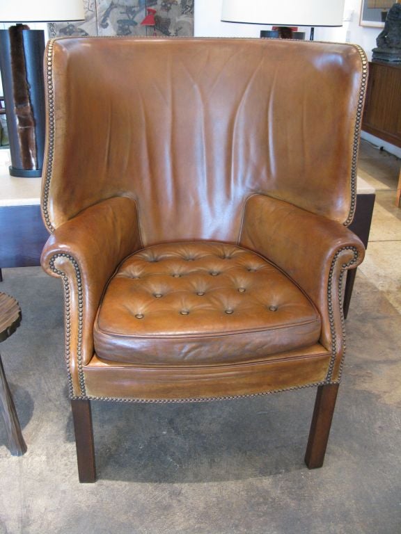 Brown leather wing back chair with beautiful curvature, tufted seat, and aged brass grommet detailing.  In the style of Fritz Henningsen.