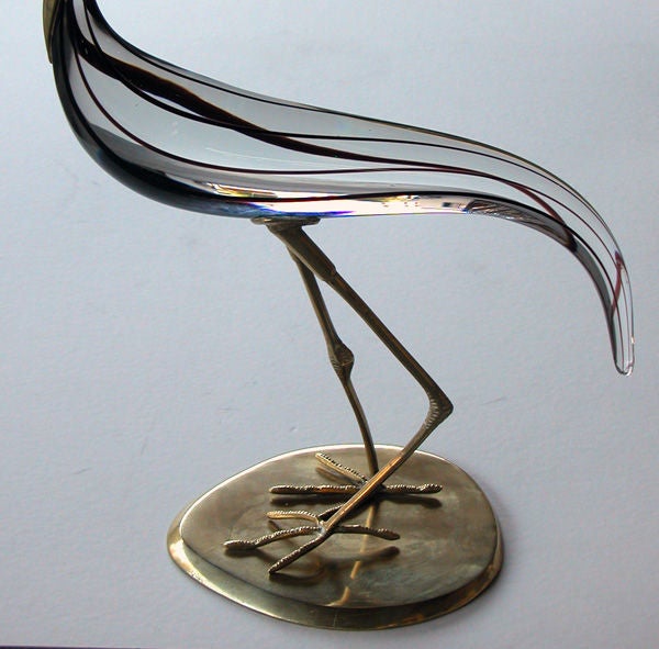 A graceful and large-scaled Italian glass crane with brass mounts; Murano; the brass head with elongated bill above a shaped clear glass body with downturned tail; supported on  2 slender brass legs over a brass plinth
