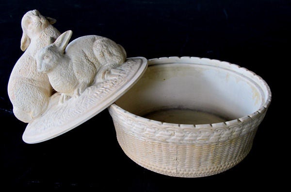 A charming French beige-colored pottery basket-weave bowl with cover adorned with two rabbits; the domed lid with one seated and one standing rabbit with inquisitive gazes; resting on a circular basket-weave bowl.