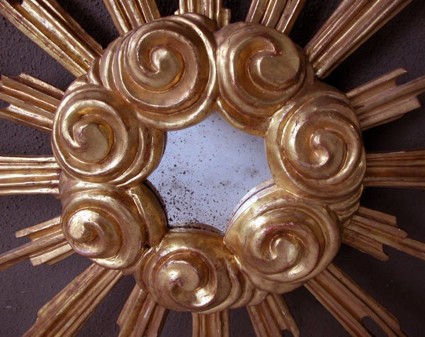 A large-scaled and boldly-carved French giltwood starburst mirror; the central mirror plate with scalloped edge within a lively cloud scroll frame; emanating radiating arms of varying lengths