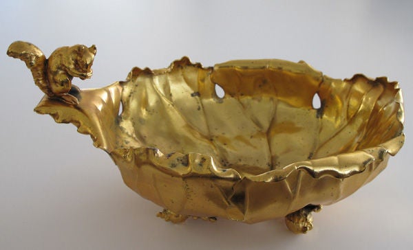 A whimsical American gold plated nut dish with figural squirrel handle; by Pairpoint Manufacturing Co.; the cabbage form dish with detailed figural handle of a squirrel holding a nut resting on miniature cabbage feet; stamped 