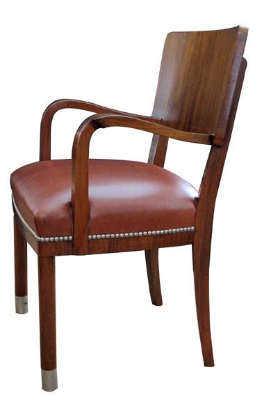 A handsome and good scaled set of 6 American 1940's ribbon-mahogany dining chairs (4 sides, 2 arms); each with rectangular incurved backrest above a bowed russett leather seat above a plain skirt; raised on round legs ending in brushed aluminum caps