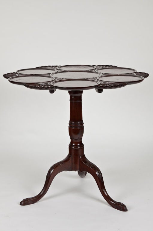 Fine George III Irish mahogany supper table, the shaped and scalloped top with richly carved details and vivid grain, standing on urn turned shaft supported by foliate carved legs standing on elongated ball and claw feet.