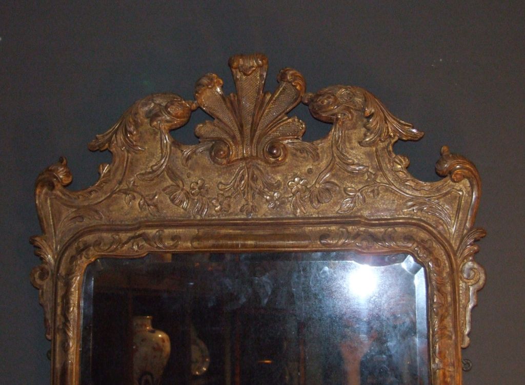 Fine George I giltwood looking glass, the eagle and foliate carved crest with punched ground surrounding an arched and shaped hollow beveled plate with raised molding, over scrolled sides and base and retaining its original glass.