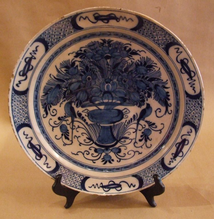 18th Century Dutch delft charger in blue and white having a diaper and squiggle lozenge border, the center with flowering urn surmounted with a pair of lovebirds perched on branches.