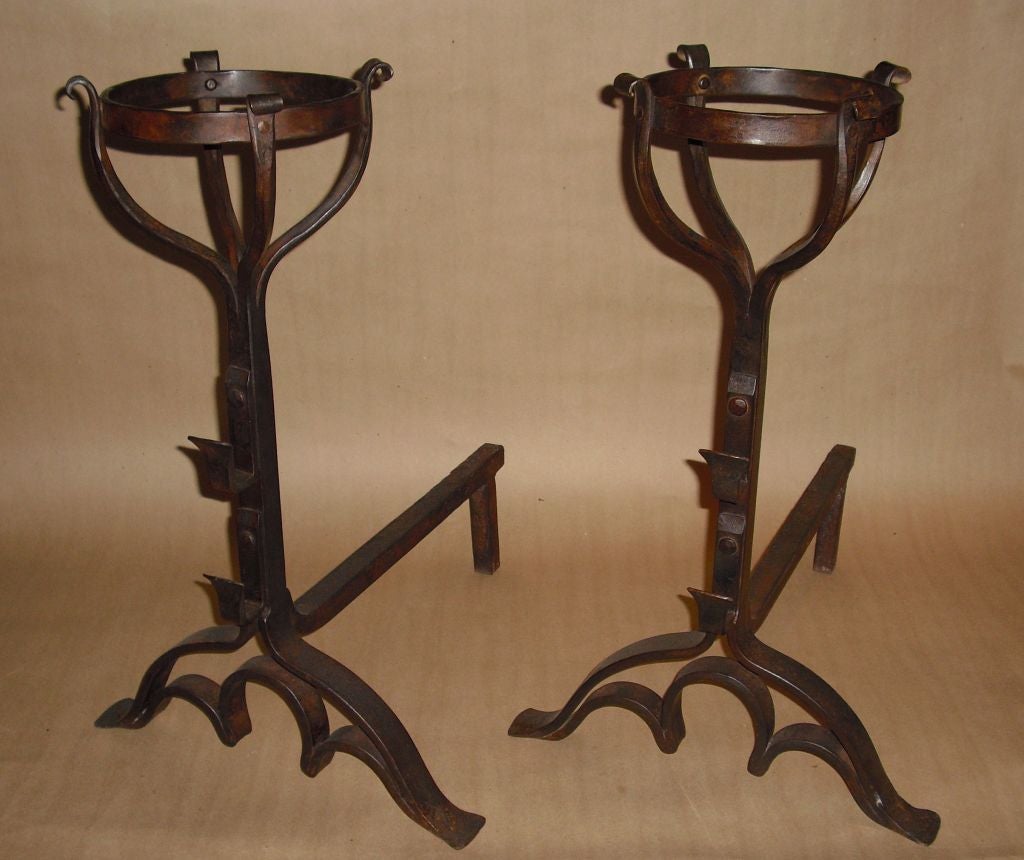 Pair of bold and masculine patinated wrought iron andirons with basket and ring tops over arched feet with Gothic tracery, good quality and weight.