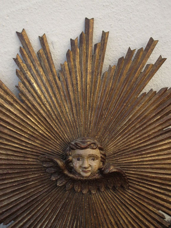 Carved and gilded wooden sunburst with carved portrait of a putti at center.