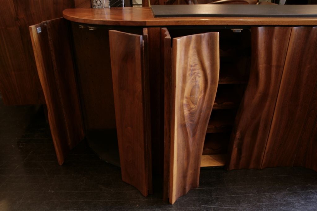 Custom Wall Mount Console by Phillip Lloyd Powell, circa 1960's, USA.  Unique carved walnut case with four pairs of bi-fold doors concealing four main compartments, one with a custom fitted wine rack, one with two drawers and shelves and glass