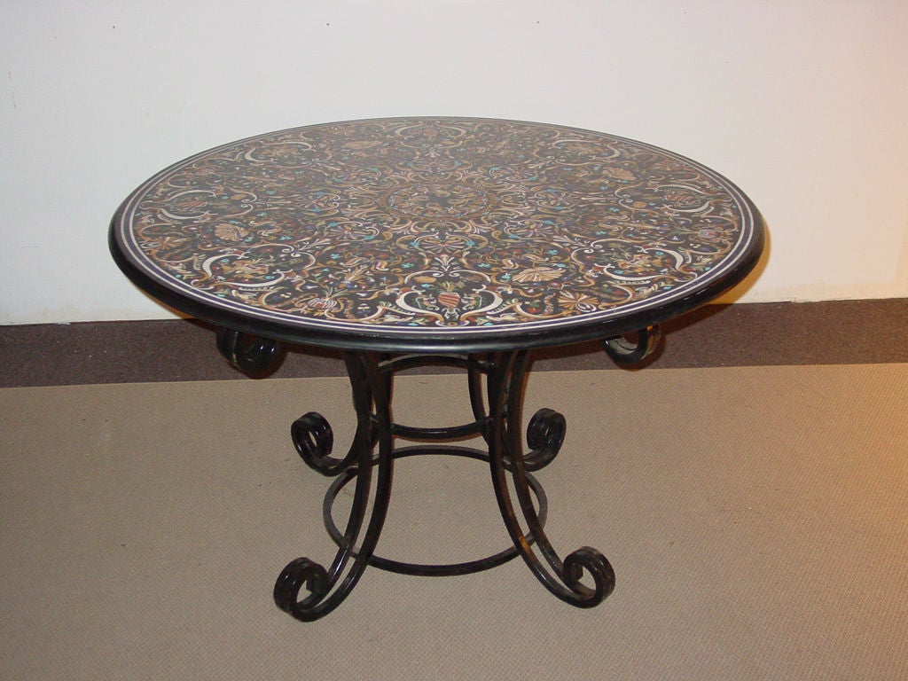 the circular molded black marble top intricately inlaid with arabesques, shells and trailing foliage with lapis, malachite, coral and various colored hardstones on  C- scrolling wrought iron base