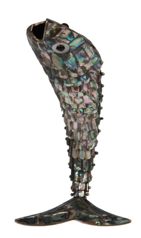 A marvelous and unusually large bottle opener shaped like a fish covered in mother-of-pearl “scales” and engineered to stand on its tail, creating movement as if jumping out of the water.  Its mouth is made of bronze and is designed to open bottles.
