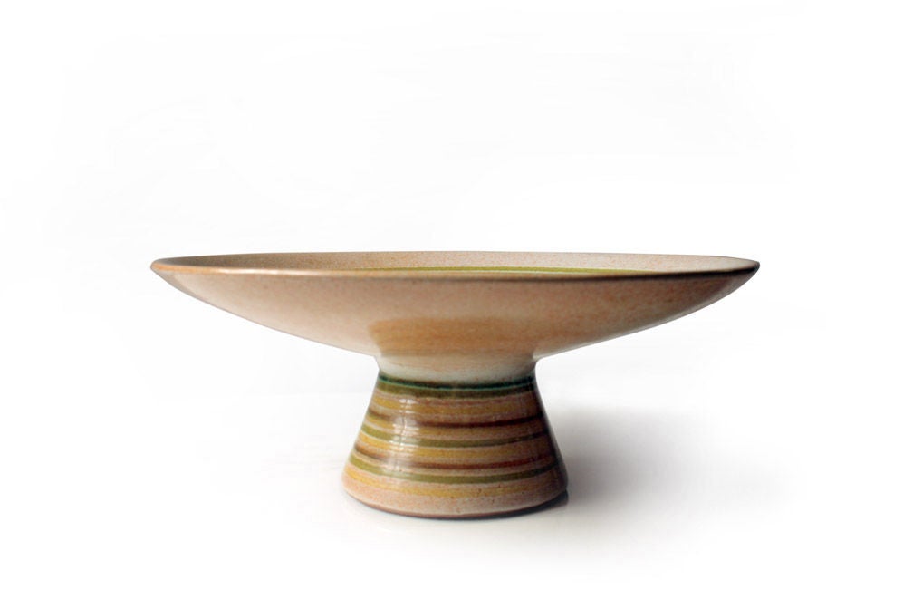 A mod ceramic compote with a shallow dish decorated with concentric circles in shades of green and yellow raised on a conical foot with similar circle motif.  By Design Technics. American, circa 1960.