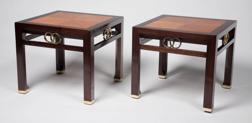 A pair of chic square occasional tables in dark stained walnut with inlays of teak reverse diamond matched veneers in alternating light and natural stained wood. Each table has accents to the apron of interlocking rings, as well as brass sabots to