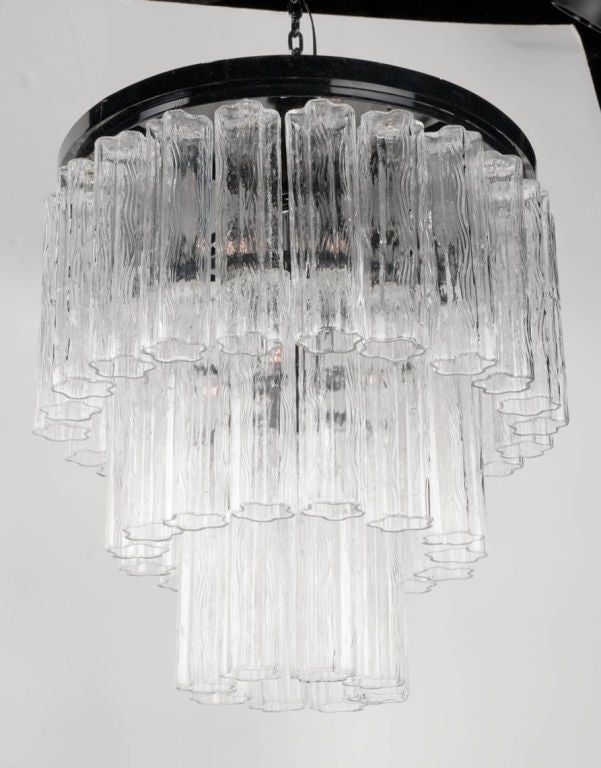 A glass tube chandelier comprising a round, black enameled steel plafonnier metal frame supporting three tiers of 45 pieces of textured molded glass tubes. By Camer Glass. Italy, circa 1970.