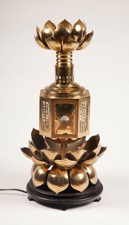 An elaborate brass lantern with a chinoiserie motif comprising lotus leaf crown atop a chased and pierced column that is supported by a pierced lantern that holds a bulb; this is supported by a brass pedestal surrounded by the lotus leaf motif,