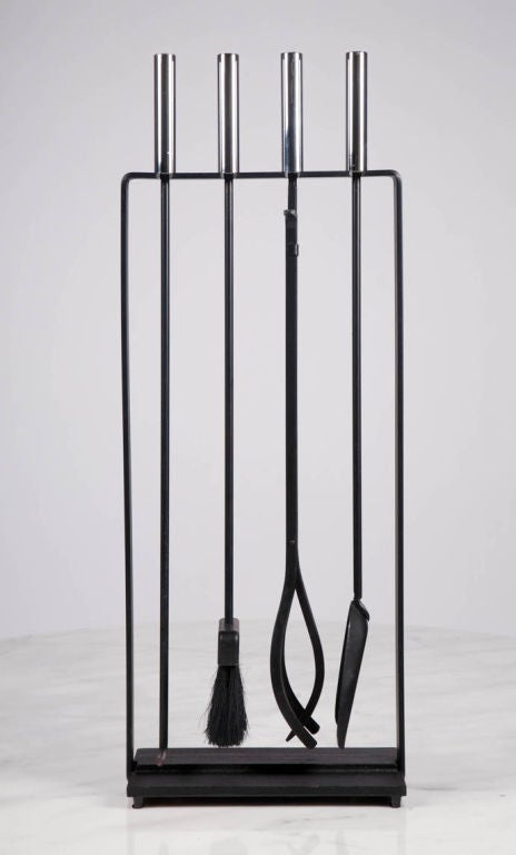 A set of four fireplace tools with integral freestanding holder in wrought iron with nickel cylindrical handles. Manufactured by Pilgrim. American, circa 1950.