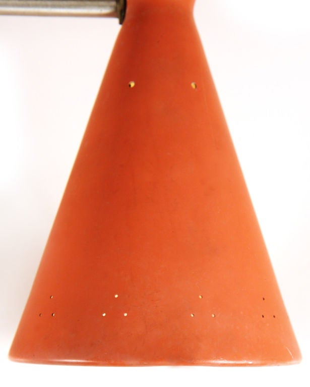 A Mid-Century Modern dual pendant light comprising a satin steel round stem supporting a pair of double cone shades in original matte dusty orange-red lacquer each with triangular patterned pin hole piercings. Three-way wiring for uplighting,