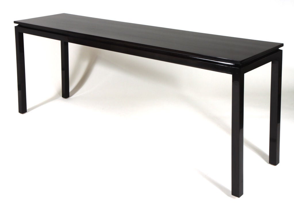 A long, tall walnut console sofa table in a clean line form with a top that appears to float over its frame and finished in a very dark stain and high gloss lacquer.  By Harvey Probber.  American, circa 1950.