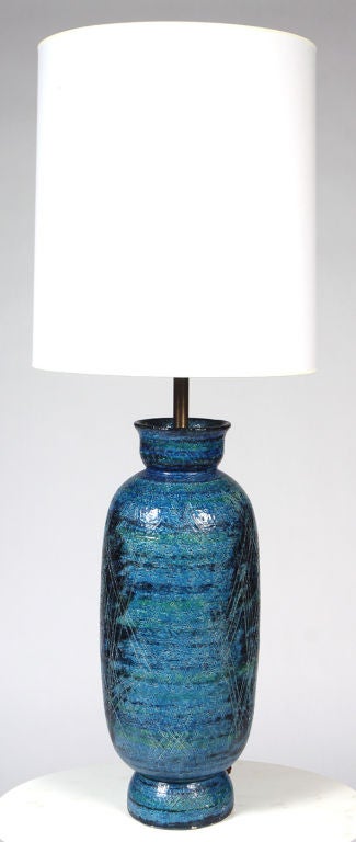 A vibrant Rimini turquoise blue glazed pottery table lamp in a bottle shape composed of a rim, a tall cylindrical body with abstract incised decoration, cupped foot and three way switch. By Aldo Londi for Bitossi. Imported by Raymor. Italian, circa