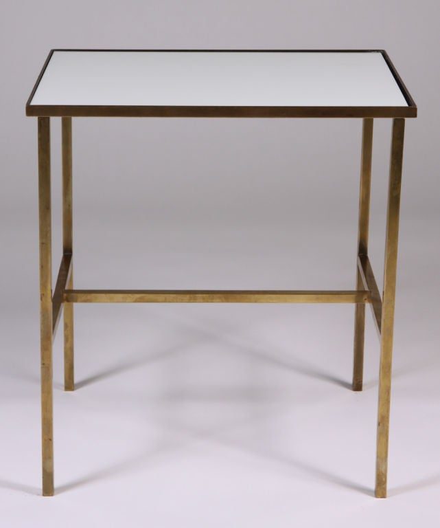 A mod telephone table with a lustrous Vitrolite glass surface inset within a rectangular polished brass frame with an H-stretcher. By Harvey Probber, American, circa 1950.