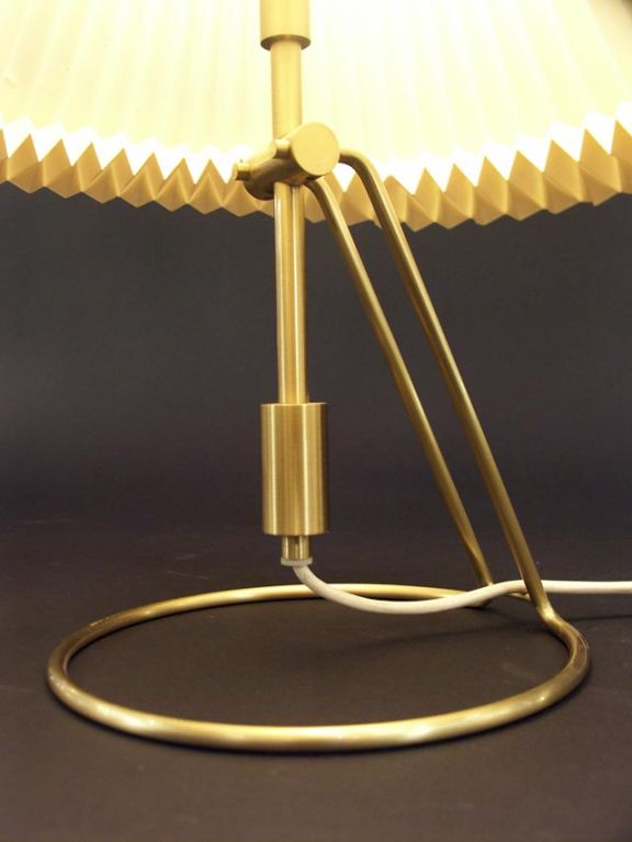 Interesting and unusual table lamp by Le Klint. An adjustable brass stem is suspended above a hoop base, and can be tilted in both directions to diffuse the light. Included is the original folded cellulose shade, pressure fitted to the base.