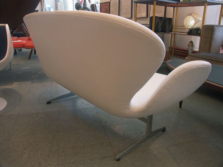 Nice example of Jacobsen's rare companion to his swan chair. The curvaceous form is extended to loveseat dimensions, losing none of its modernist character in the process. newly reupholstered in supple white leather.