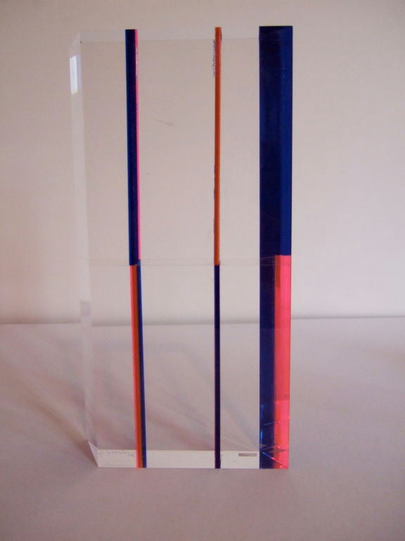 Clear flat lucite sculpture with blue and hot pink bands of color.  The sculpture is not a perfect rectangle, the sides are cut at angles so it is more of a 3-d parallelogram.  Signed, 