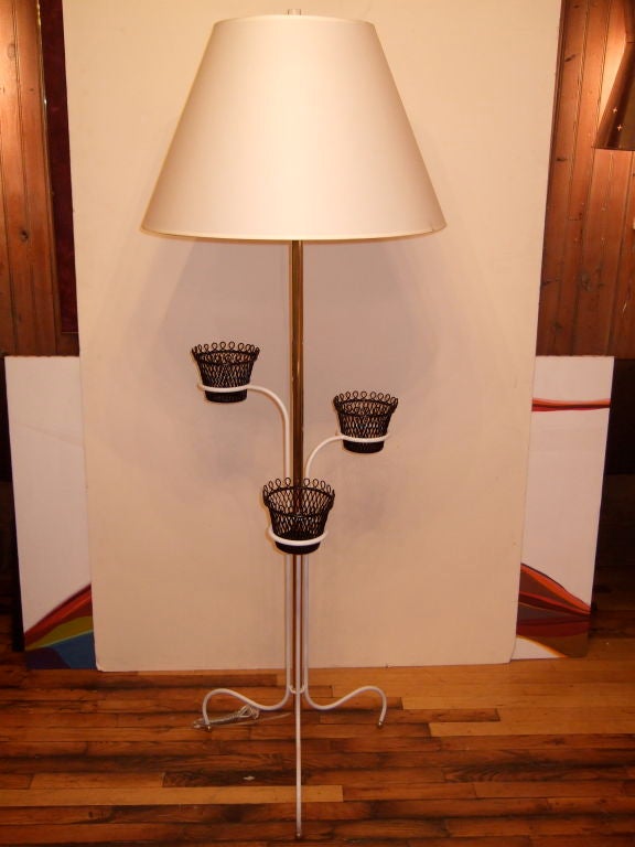 Mathieu Matégot floor lamp. Lacquered white tripod base perched on brass ball feet. Three black wire flower pot holders rise up from the base. Brass tube extends up from the tripod base to the socket. Shade not included.

  