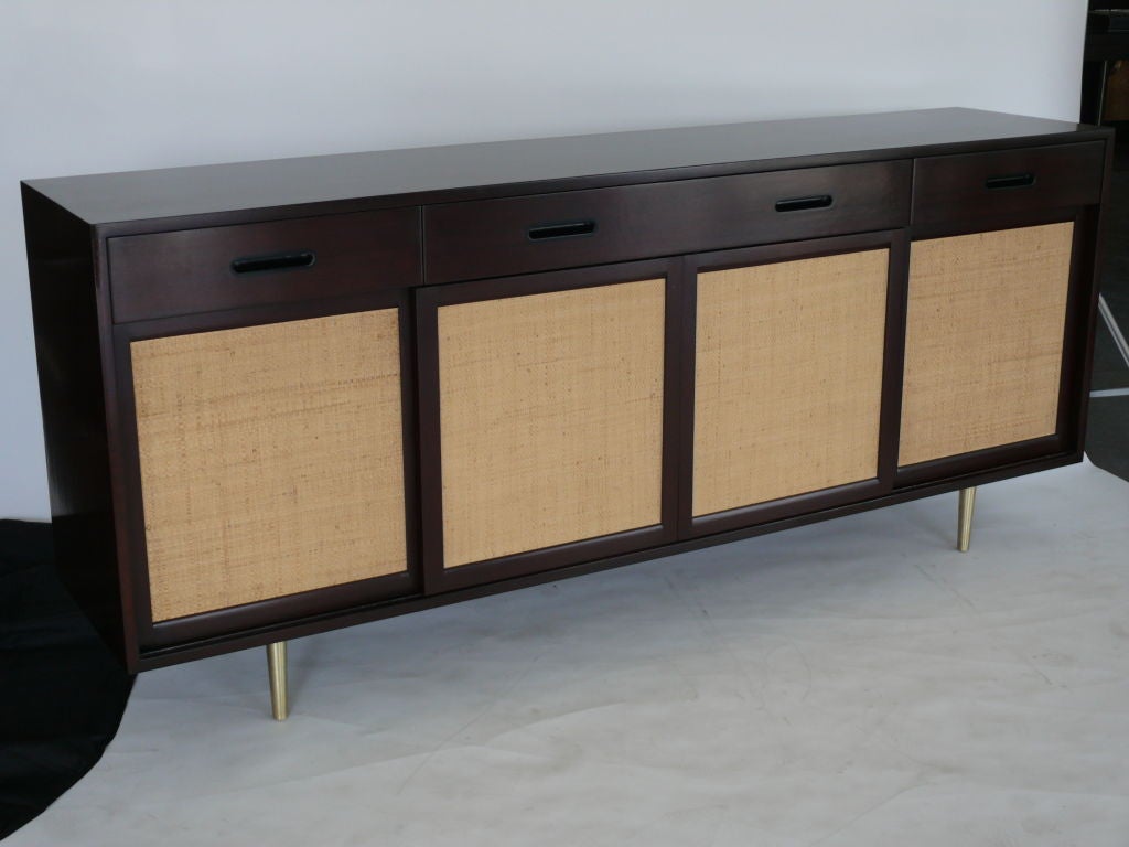 Beautiful Dunbar credenza by Edward Wormely with woven caned sliding doors, open shelving and five drawers on left side. Sits on 4 new solid brass tapered legs. Professionally refinished.