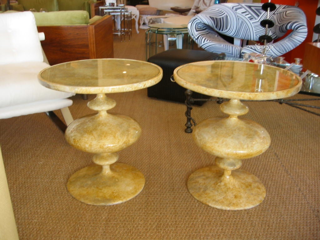 Very exciting pair of side tables fashioned in resin composition with circular glass tops which rest within the rim offering a flush top. Original faux painted finish.