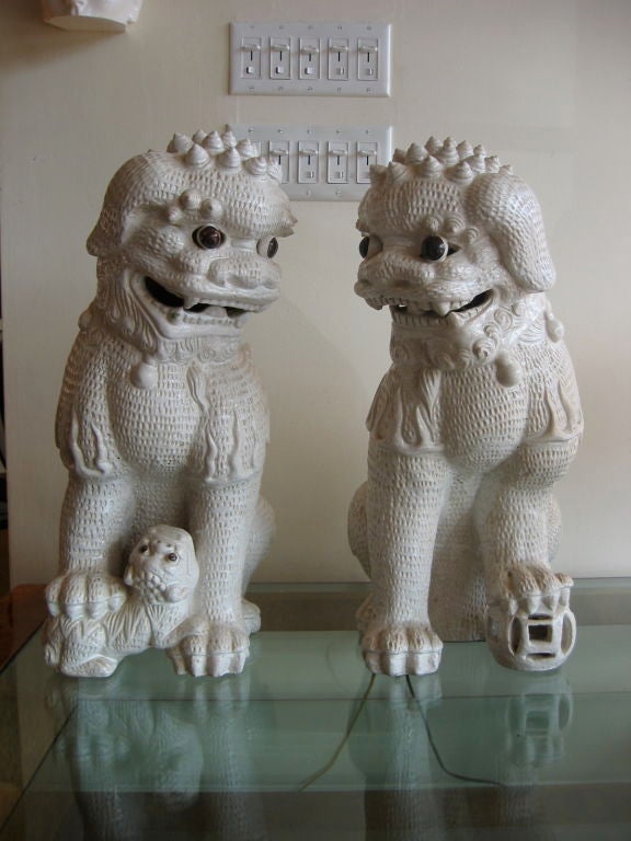 Pair of white ceramic Foo Dogs with a lot of texturing and intricate design work. Black painted eyes and one dog with pup. The Asian Foo Dog is known to bring good luck, especially when placed on either side of an entrance. Sold as a pair.
