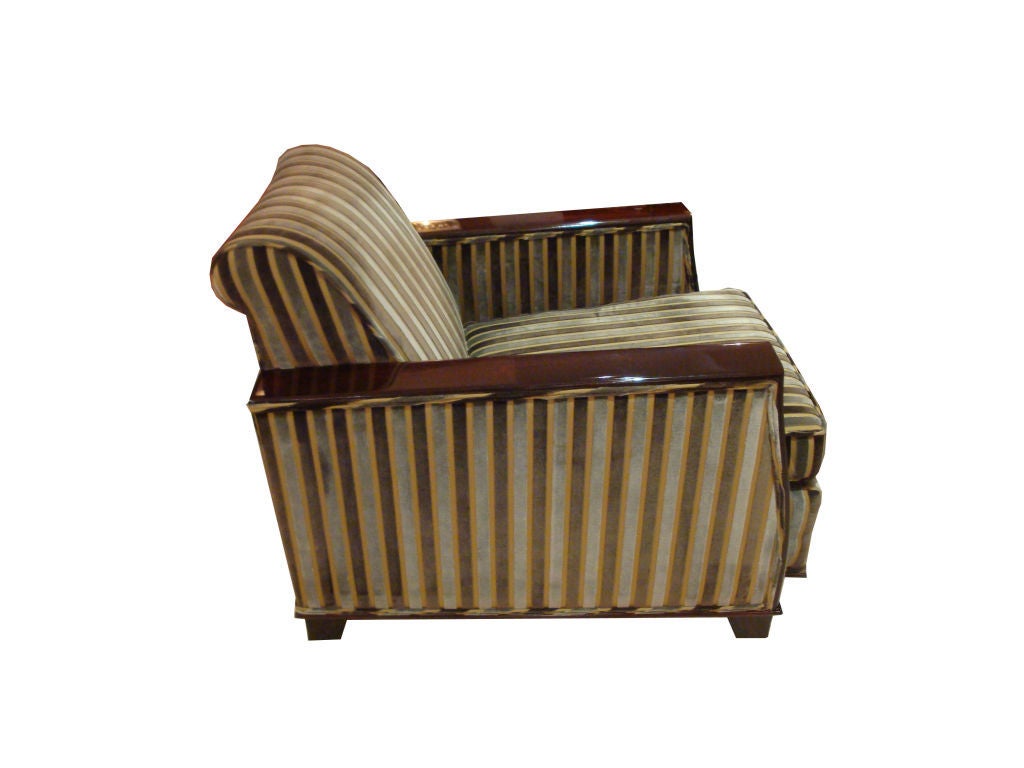 A pair of Art Deco club chairs each featuring classic art deco lines with Mahogany covered arms and curving arm fronts as well as shaped Mahogany feet. The chairs also feature deep seats, a slightly scrolling backrest and loose seat cushion. The