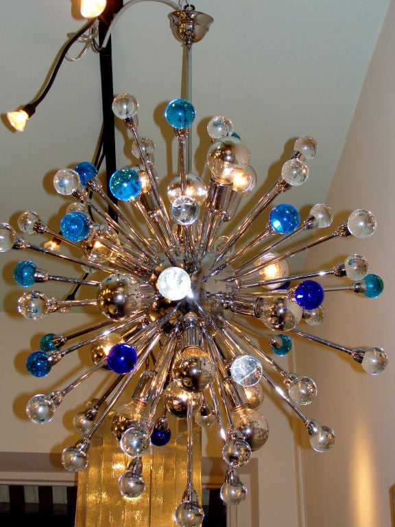 The central chromed sphere launches numerous rods of different lenght ending in full glass spheres. Mostof the spheres are clear glass, some are light blue and a handful violet. 16 light sockets of different length.