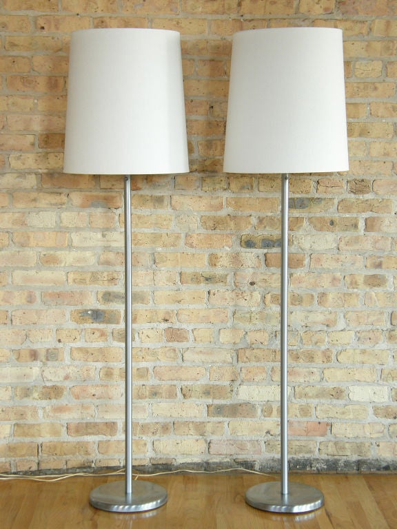 This pair of floor lamps is a classic design from Nessen Studios, NY. They have a brushed nickel finish, round bases, standard stems, and push button switches. They have an elegant, modern simplicity that will work with various different
