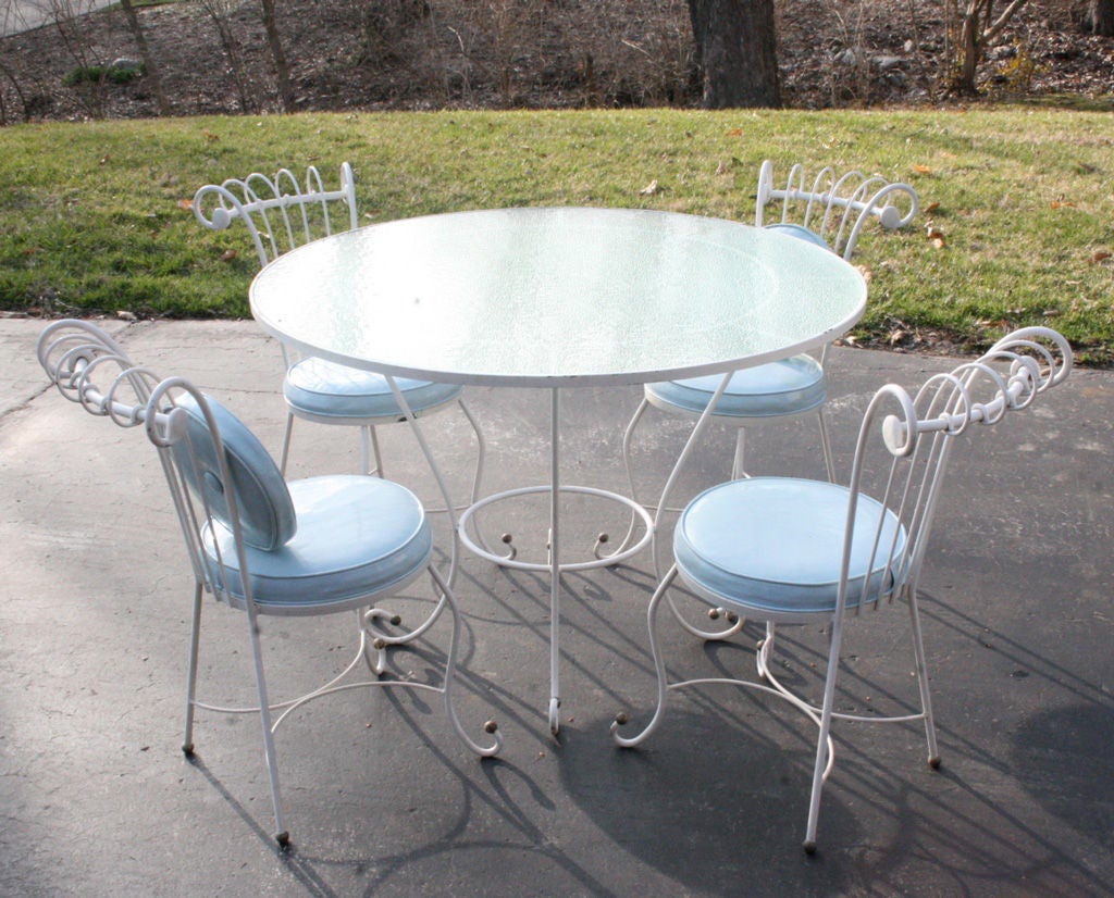 Hollywood Regency style wrought iron patio set, table with glass top, stylized iron form with ball details. Paint shows age, rust. Should be repainted. Can be sandblasted, dipped and repainted for $400. Great Mid-Century set. 

Measures: Table