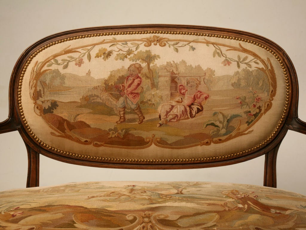 A petite (less than 4' in width) French Louis XVI fruit wood canape´, upholstered with it's original Aubusson tapestry in incredible condition for its age. This fully restored settee features a desirable oval backrest with a channeled frame and nail