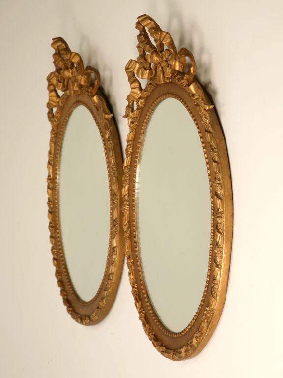 Splendid pair of original antique French oval carved and gilded picture frames with new mirror creatively put behind the original wavy glasses. Very charming with a ribbon and tassel motif, this pair are awesome as mirrors, though if you choose,