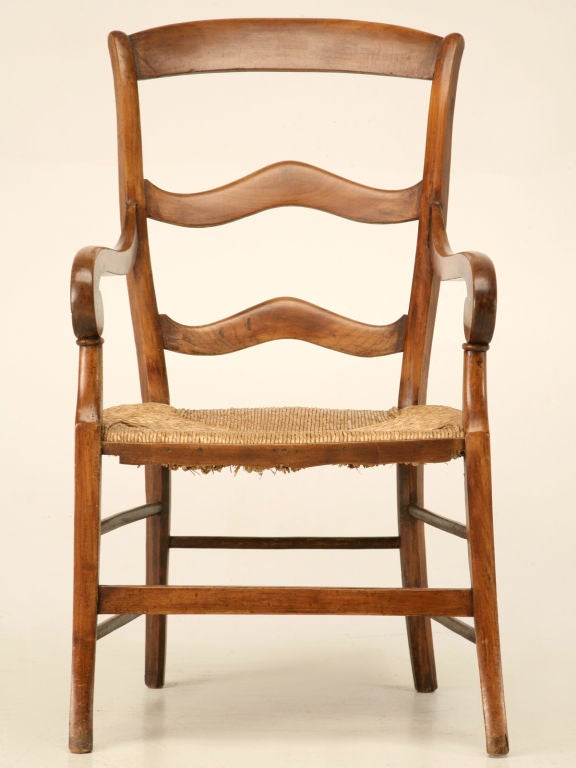 Original antique French cherrywood, farmhouse fauteuil with a rush seat, a unique ladder-back, and rolled armrests, too. If you've never experienced sitting in one of these fine chairs, you are in for a real treat, as basic as it looks, it's
